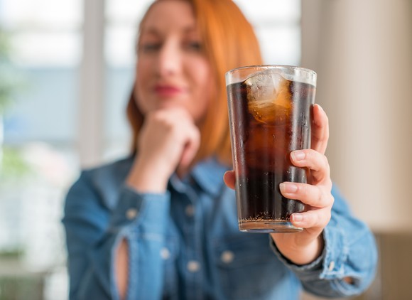 Person holding cup filled with beverage and ice cubes.