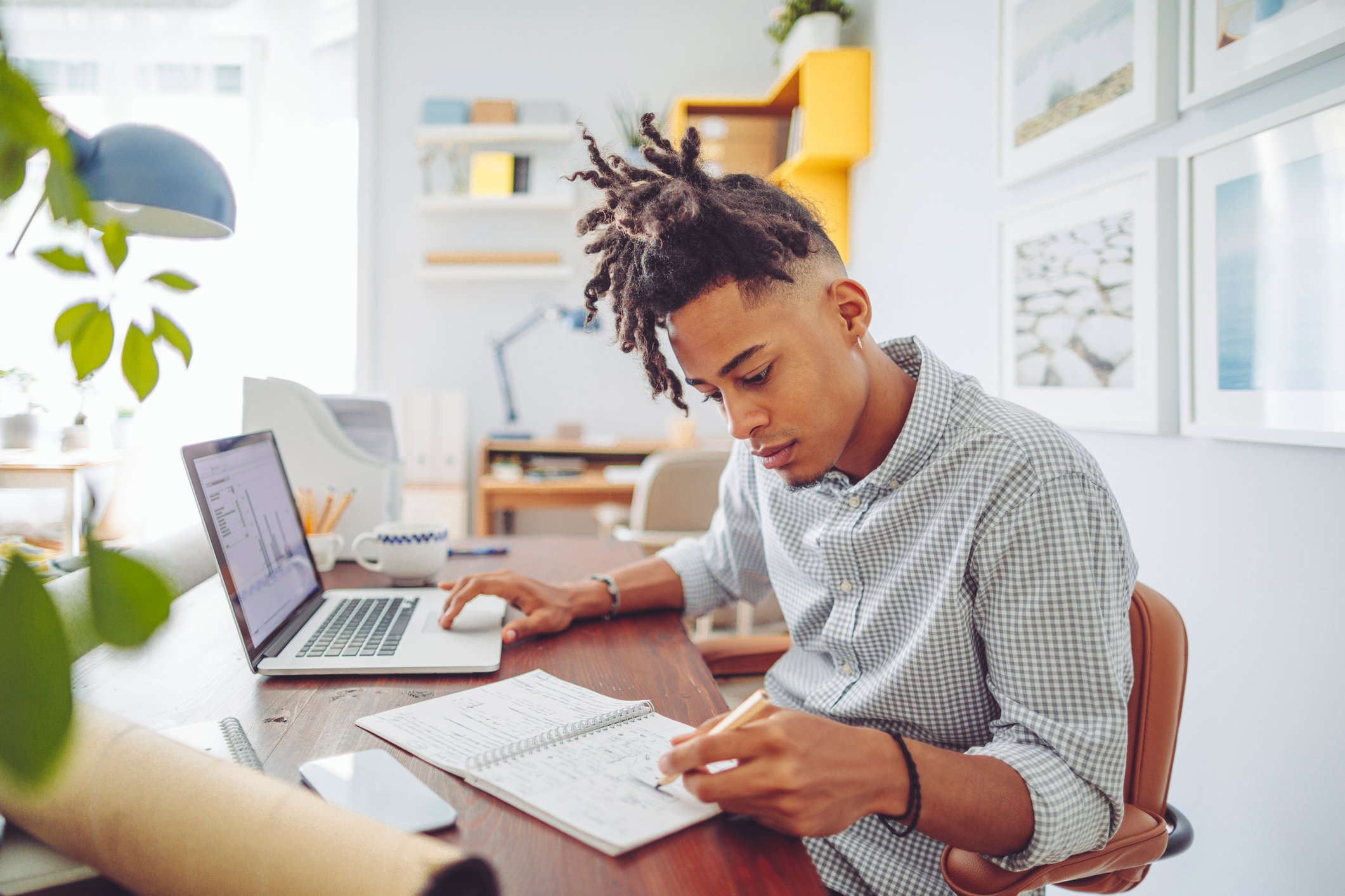 An investor studies something in a notebook and works on a laptop at home.