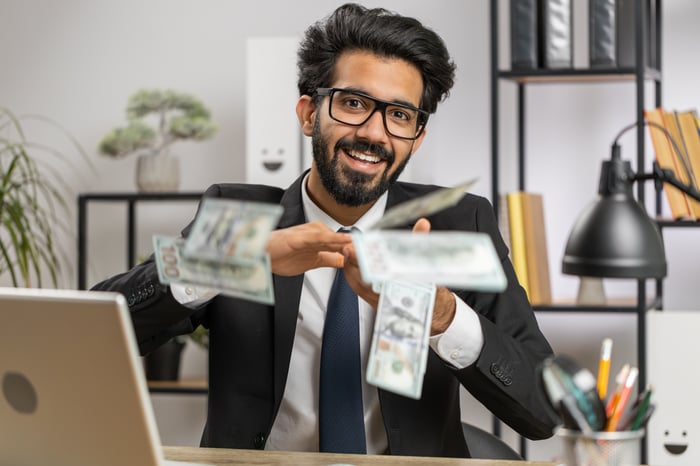 Happy person in suit throwing dollar bills at desk. 