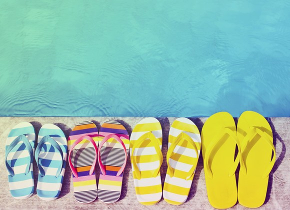 Four brightly colored pairs of flip flops lined up next to each other by the edge of a pool.
