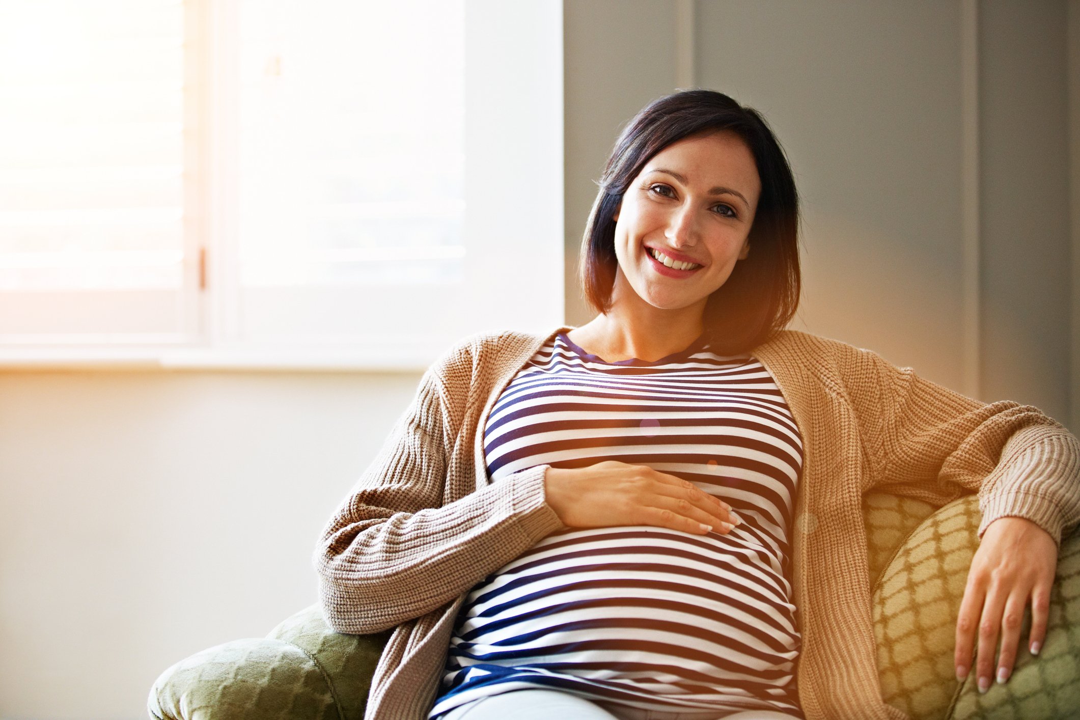 A pregnant person sitting on a couch and smiling.
