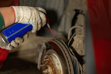 Mechanic spraying WD-40 on a car rotor.