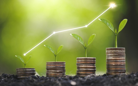 Saplings sprout from increasingly taller stacks of coins with an upward sloping line chart hovering above the saplings. 