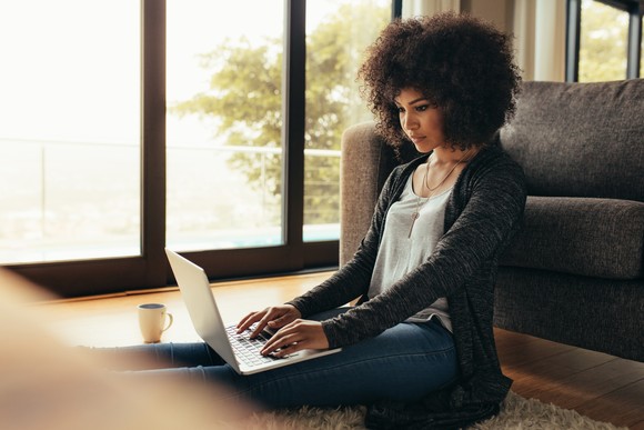 Person sitting on floor typing on laptop.