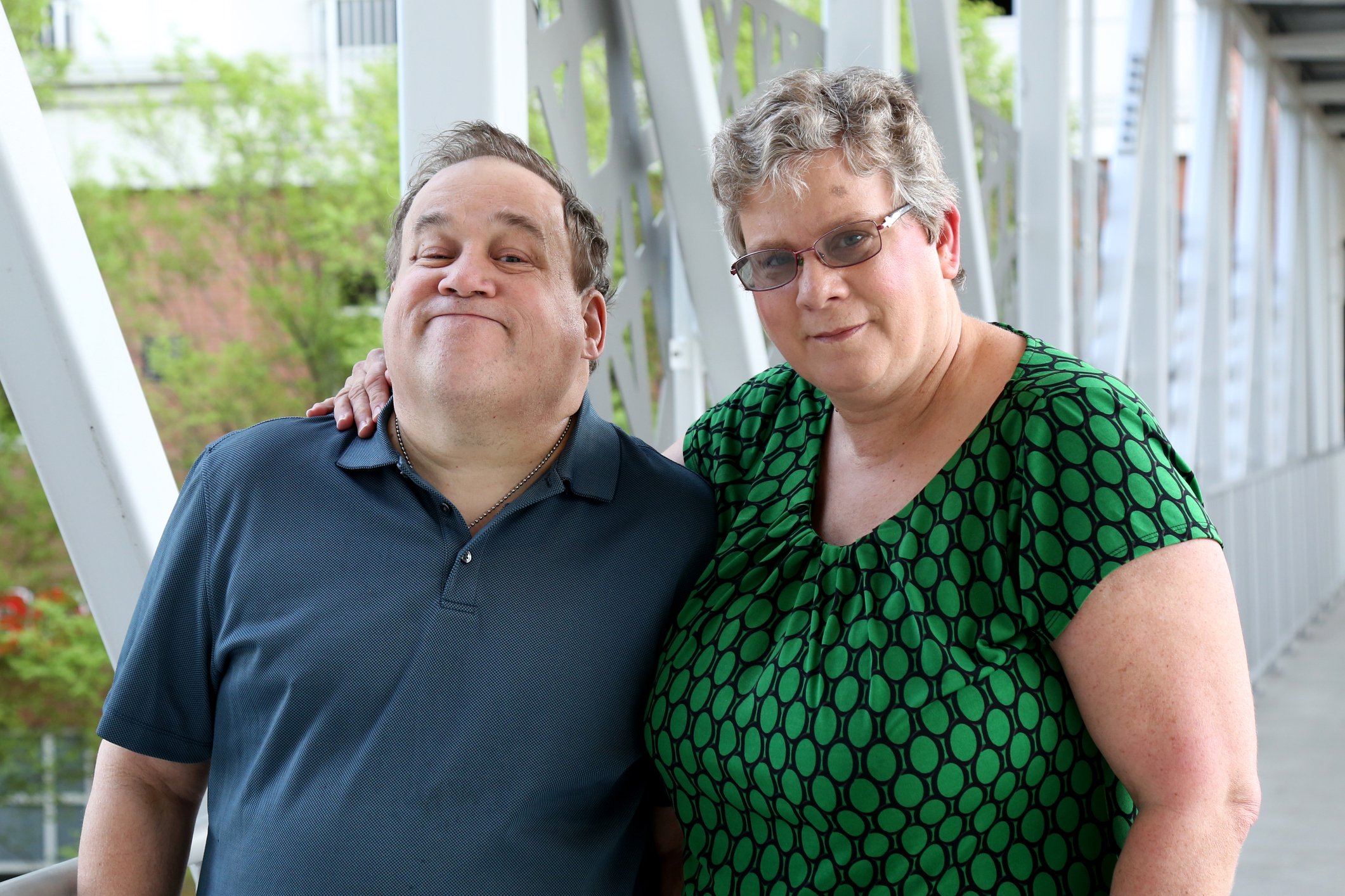 Two people are standing in a walkway, smiling slightly. 