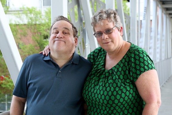 Two people are standing in a walkway, smiling slightly. 