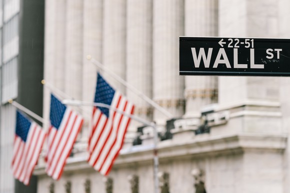 The Wall St. street sign in front of a columned building with American flags hanging from it.