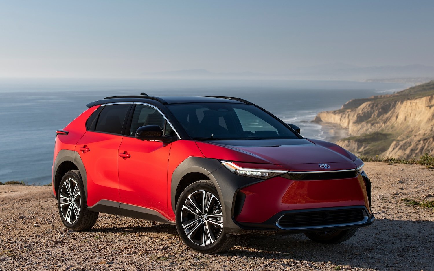 A red Toyota bZ4X, a compact electric crossover SUV, on a beach. 