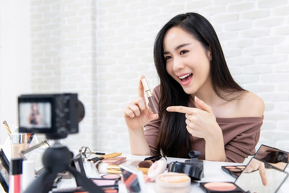 Smiling person recording themselves showing makeup and personal care products. 