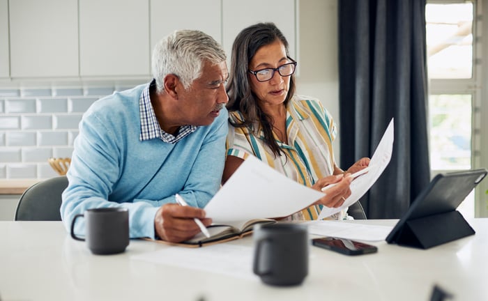 Two people at the kitchen table, looking at documents.