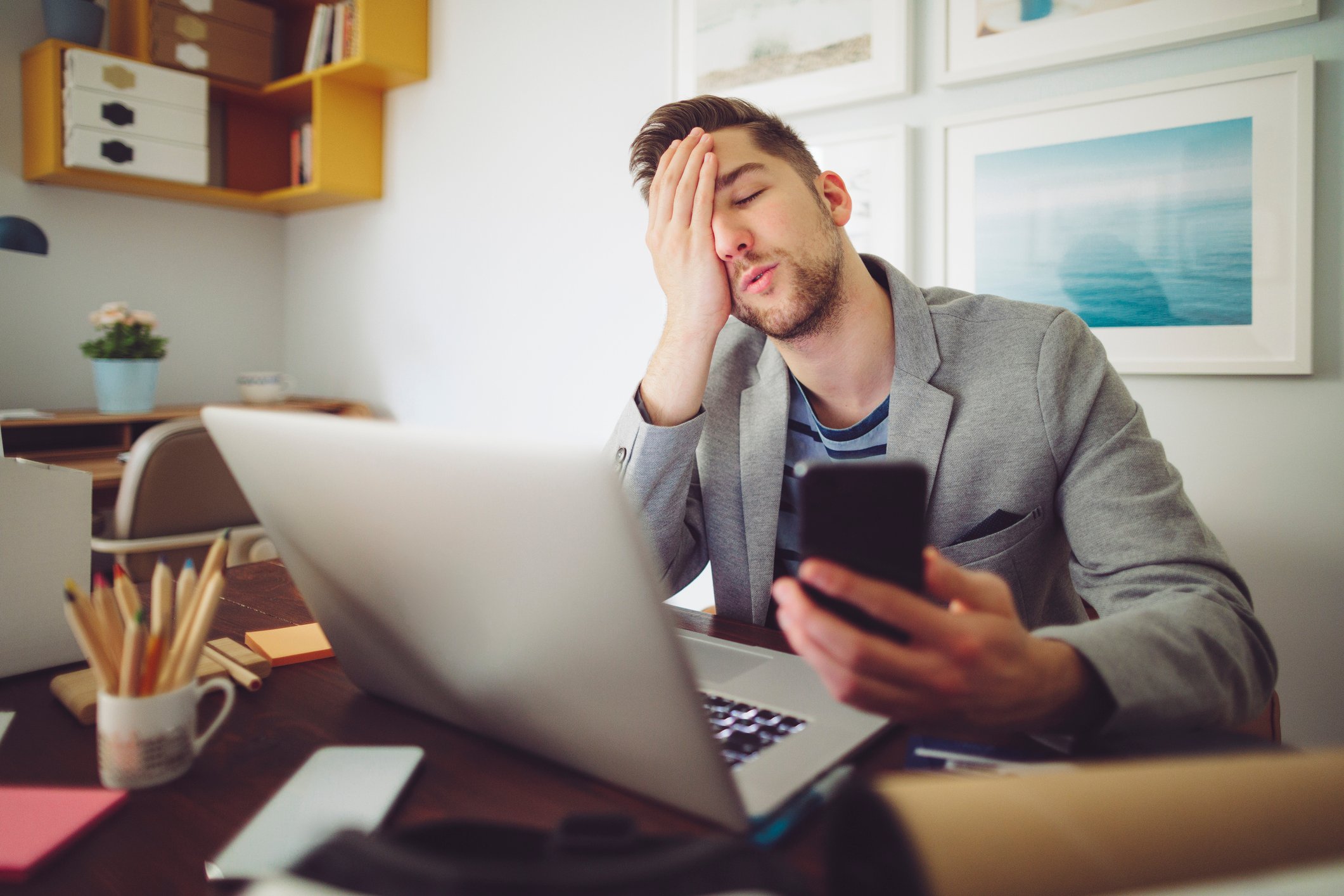 An exasperated investor sits at a laptop while holding a cell phone.