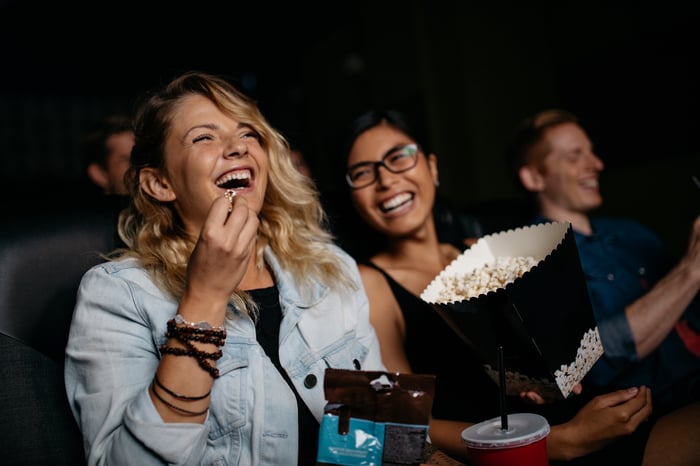 Friends laughing at the theater as they share popcorn.