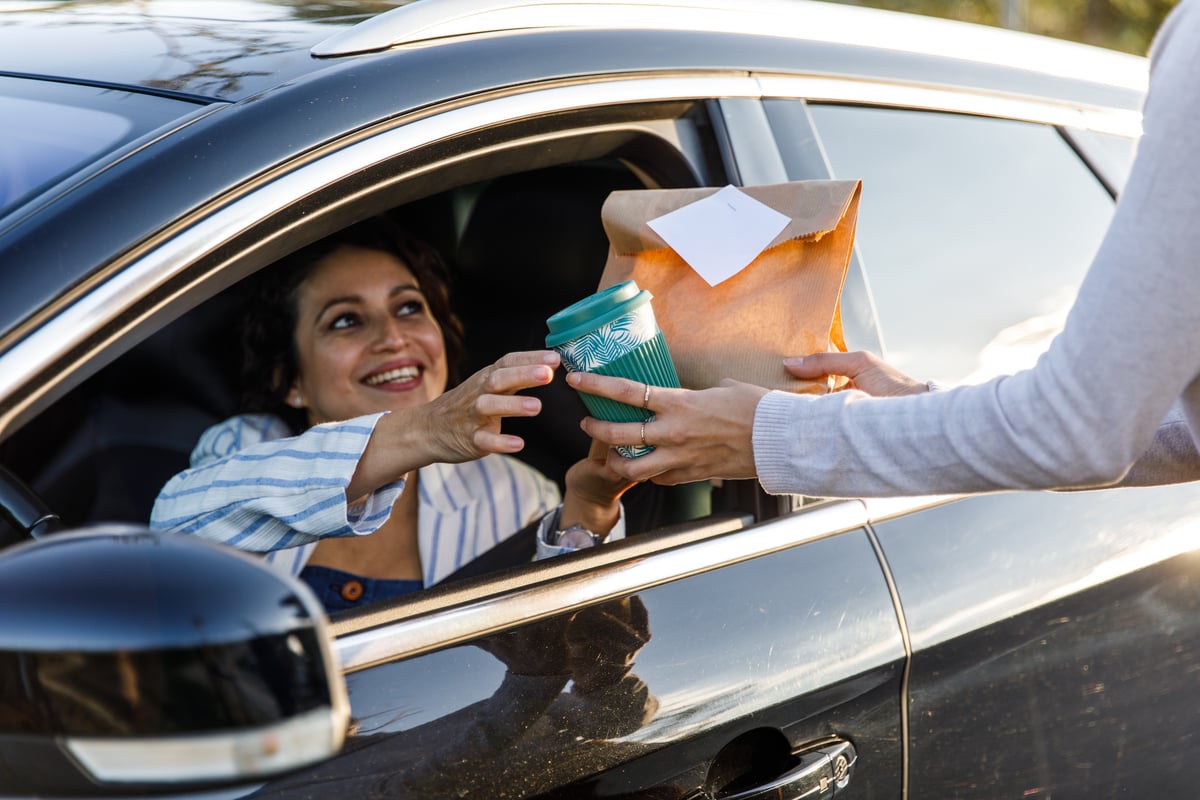 A woman receiving a coffee order in her car.