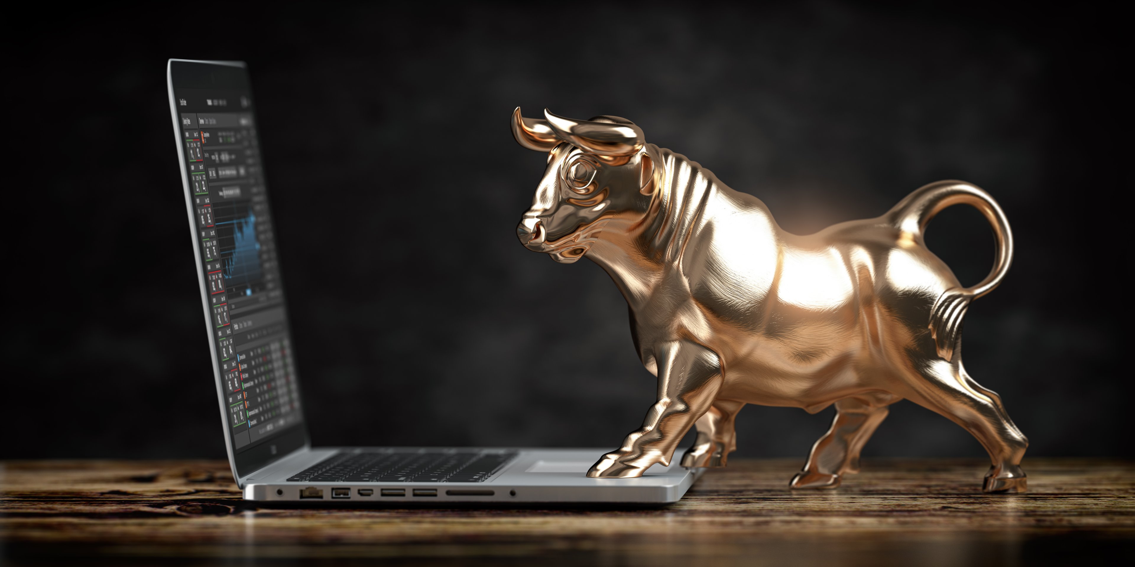 A golden bull statue trading stocks on a laptop. 
