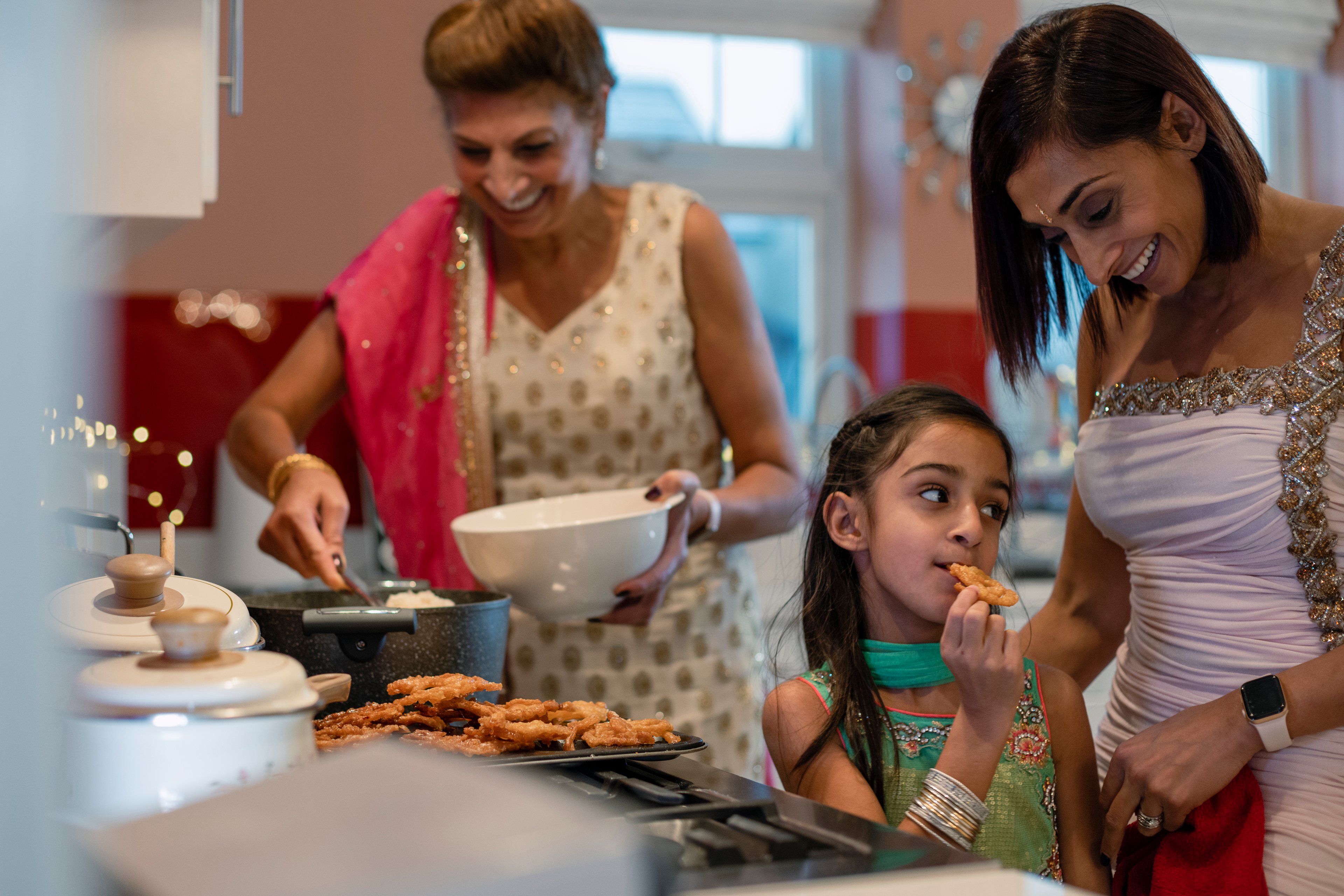Three people in a kitchen cooking and eating.