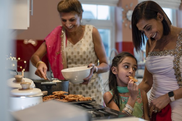 Three people in a kitchen cooking and eating.