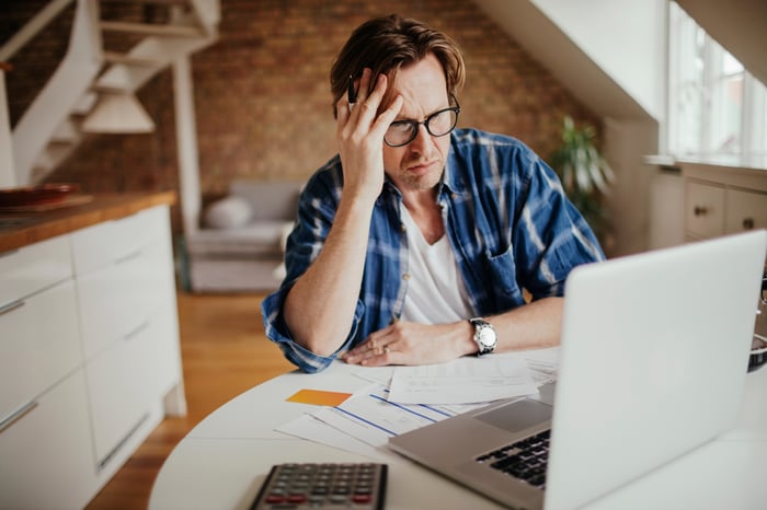 Stressed person with hand on head looking at laptop.