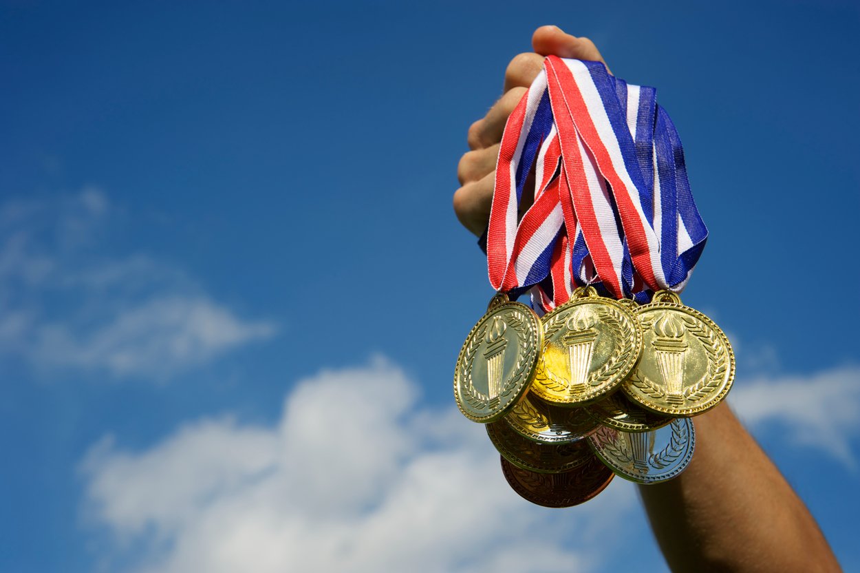 Extended human arm grasping multiple award medals in hand.