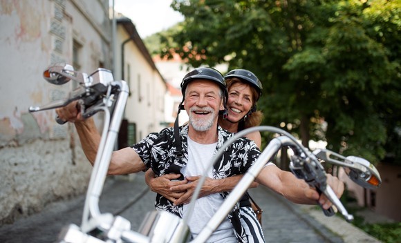 A couple is smiling while riding a motorcycle.