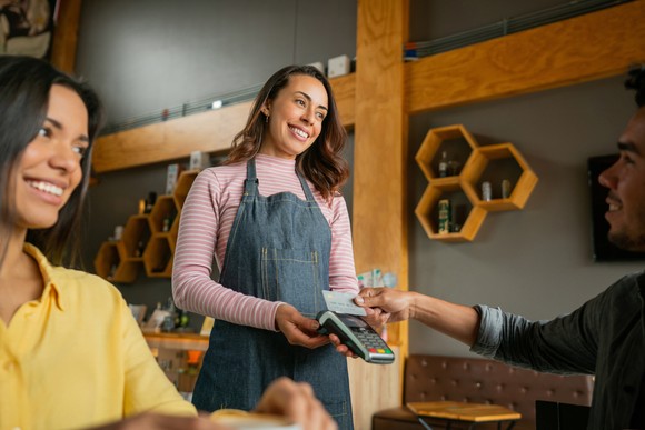 Two people making a credit card payment to a server in a cafe.