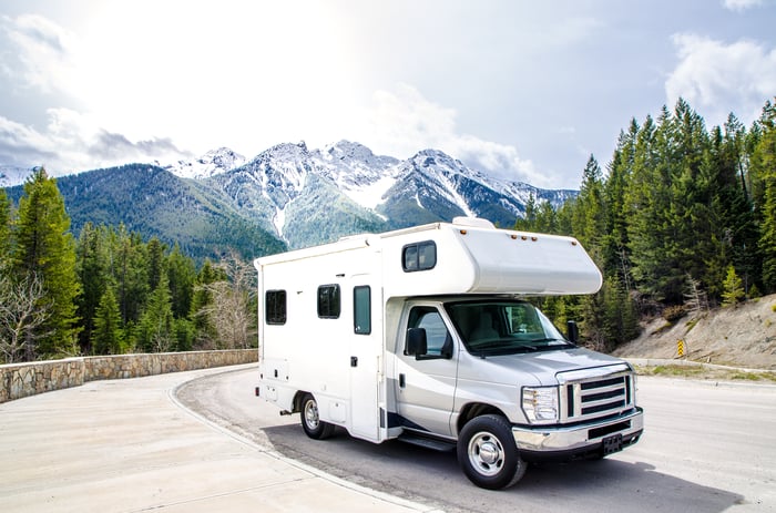 An RV travels against the backdrop of mountains.