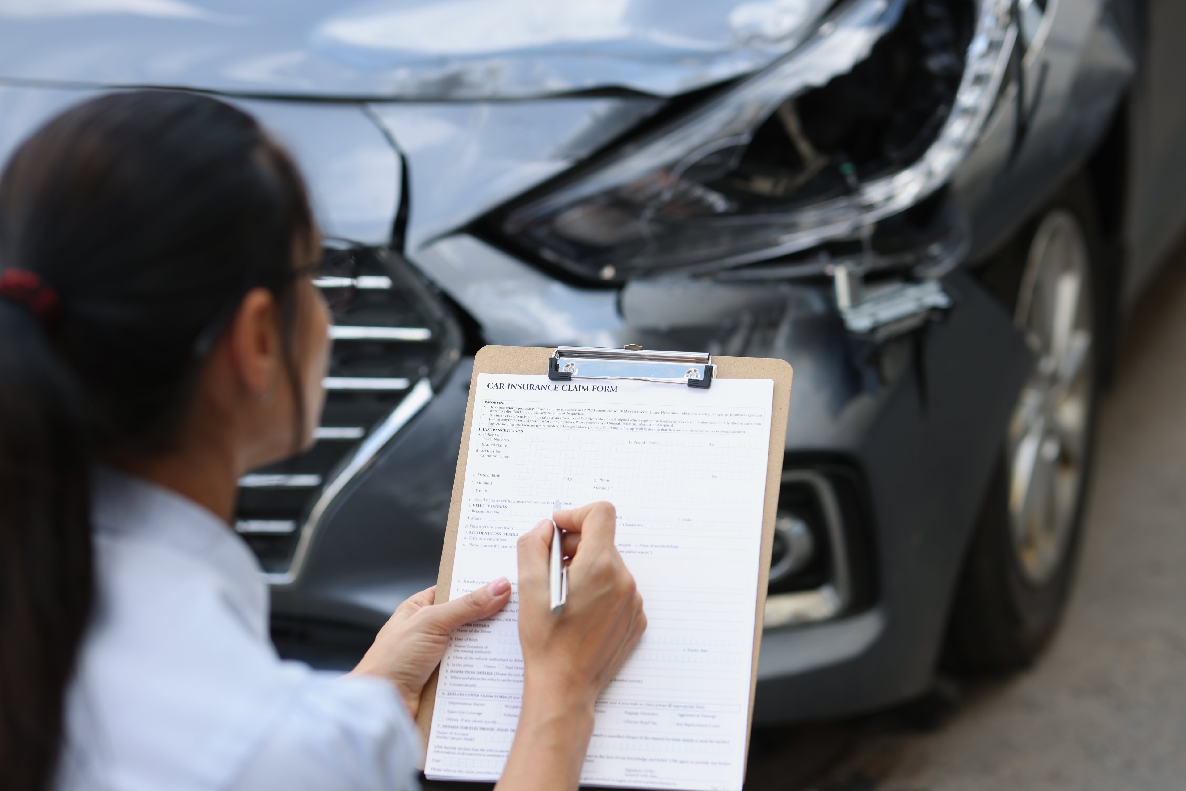 Insurance adjustor filling out paperwork while looking at car. 