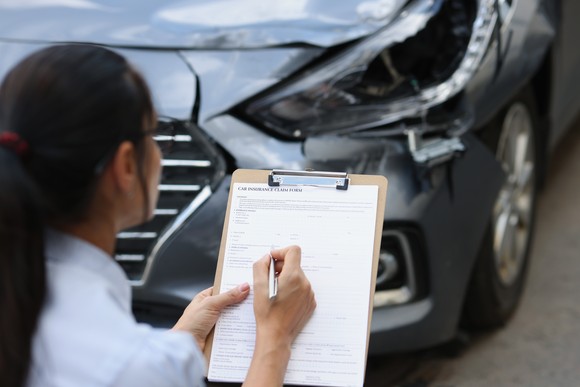 Insurance adjustor filling out paperwork while looking at car. 