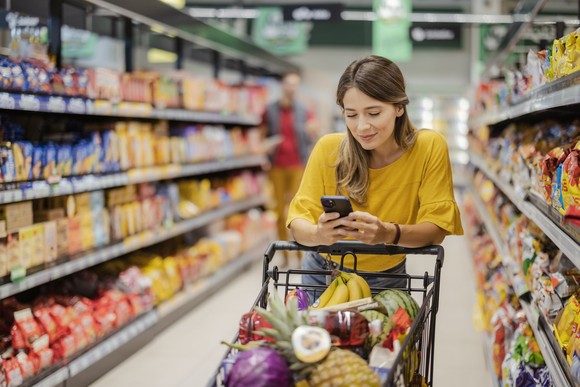 Person checking a smartphone while pushing a shopping cart in a store.