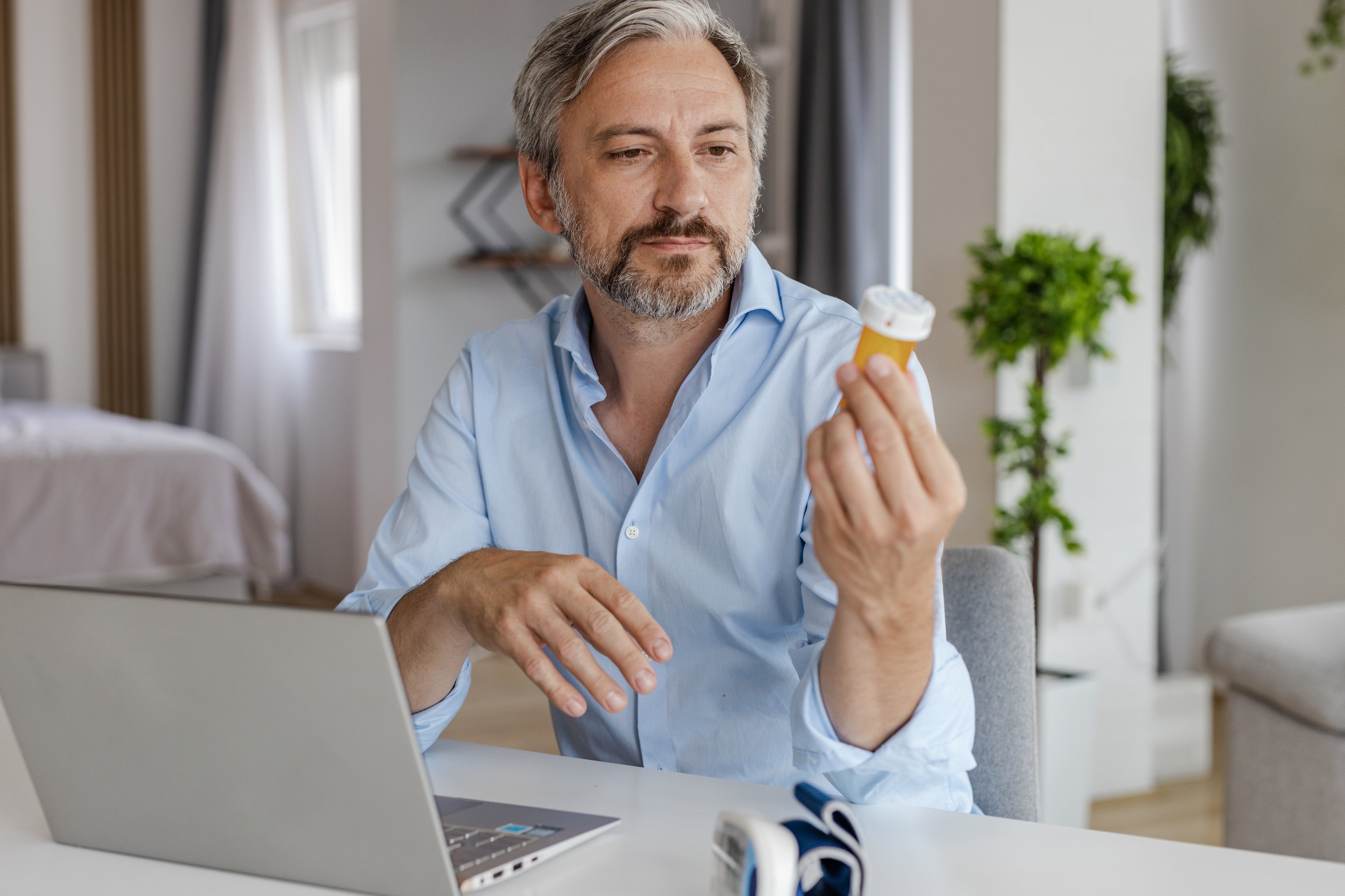 Person sitting at laptop and holding pill bottle.