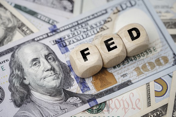 Dice spelling out "FED" for Federal Reserve on top of several bills.