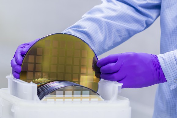 Technician handles circular semiconductor wafers. 