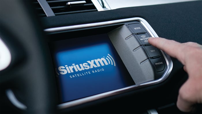 A person pushing a button on a car's dashboard to access the Sirius XM satellite radio service.