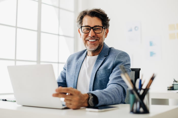 A smiling person at a laptop.