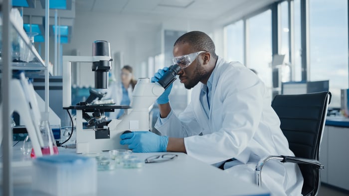 A pharmaceutical scientist in a laboratory inspecting something with a microscope.