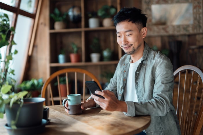 Someone is seated with a mug and is smiling at his phone.