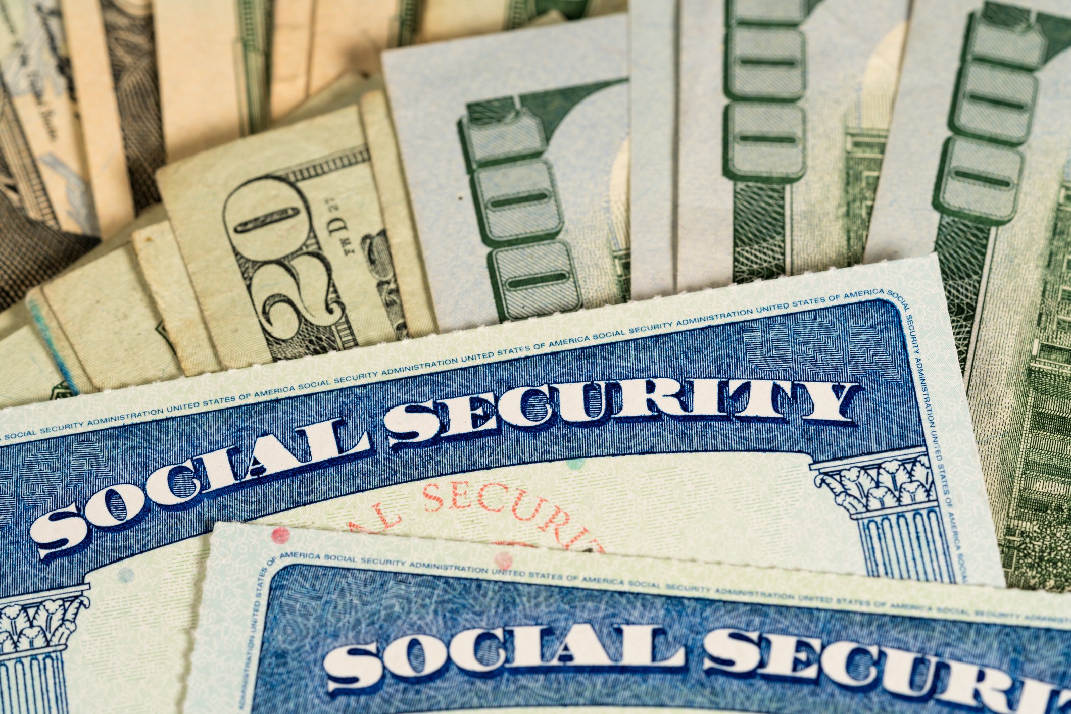Two Social Security cards laying on top of a pile of cash.