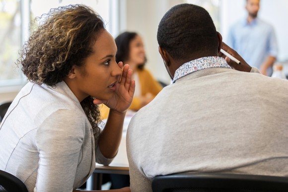 Office workers whispering secrets in a conference room.