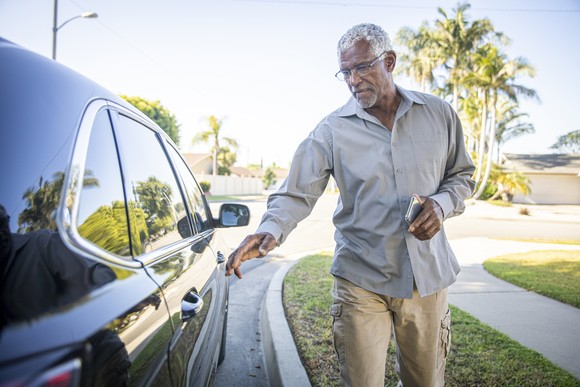 A person reaches for the door to the back seat of a car.