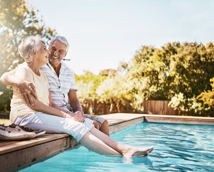 Smiling couple sitting on the side of a pool.