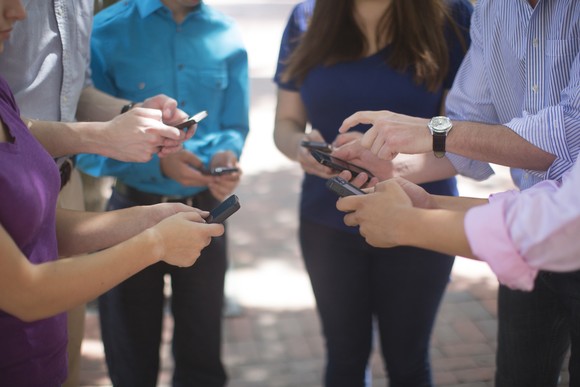 A group of people standing around using their smartphones.