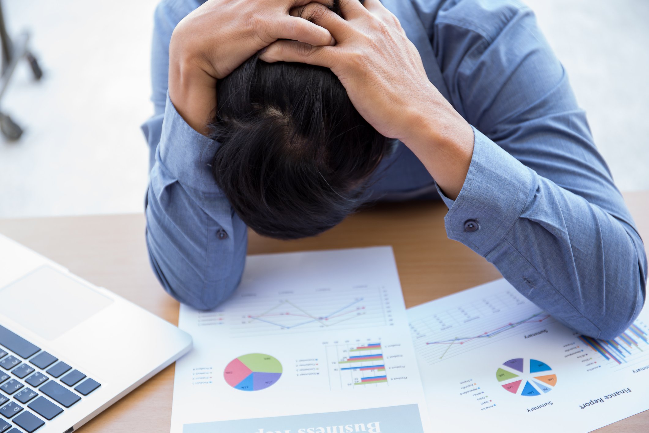 Man at desk with head down atop graph printouts
