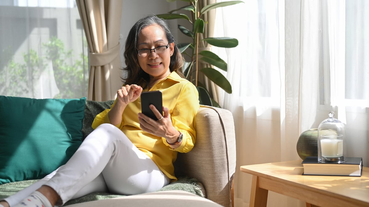 A person on a couch smiles while on a phone. 