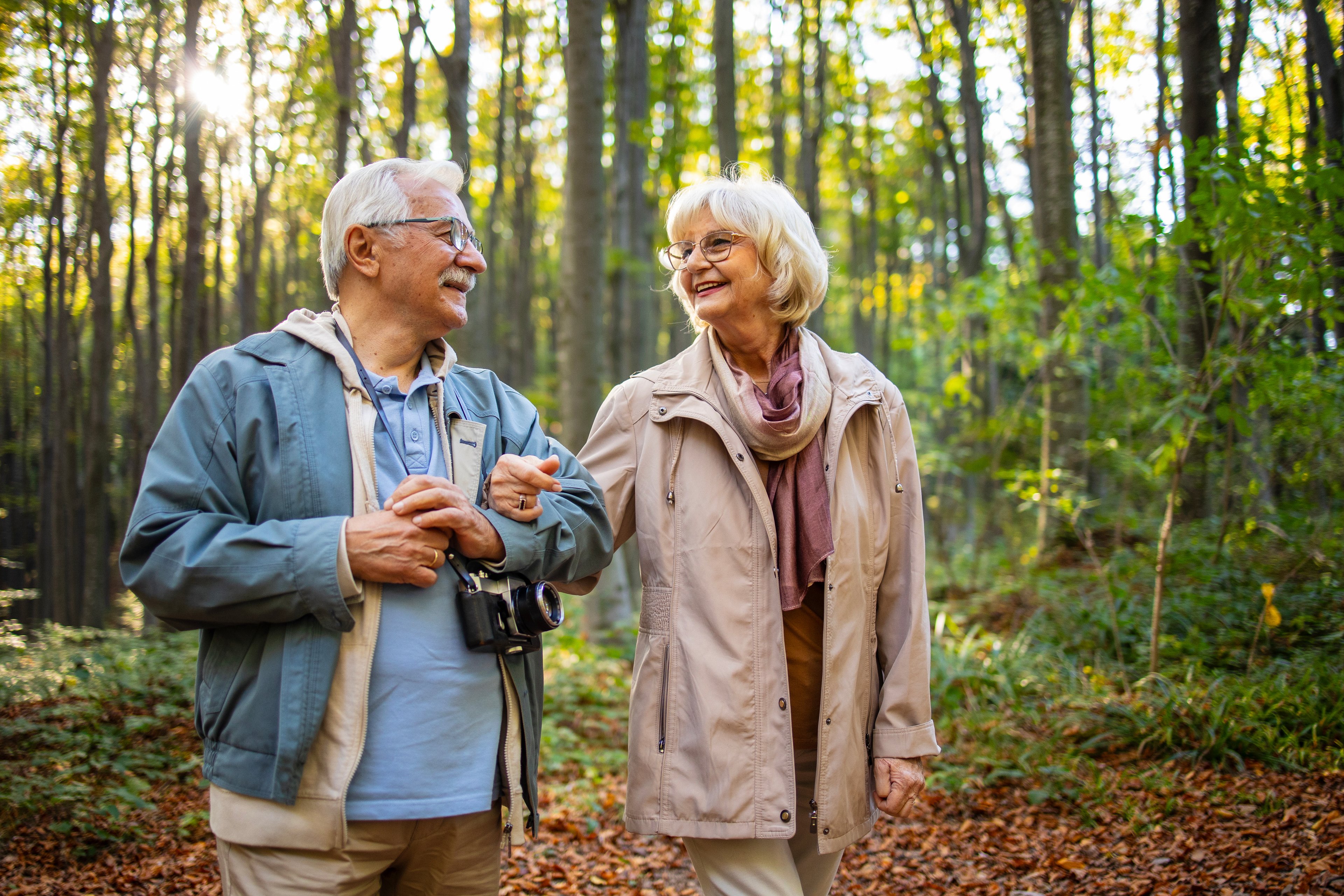 Two people in a wooded area while one has a camera.