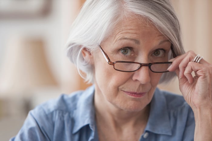 A person looking over eyeglasses while holding the glasses.