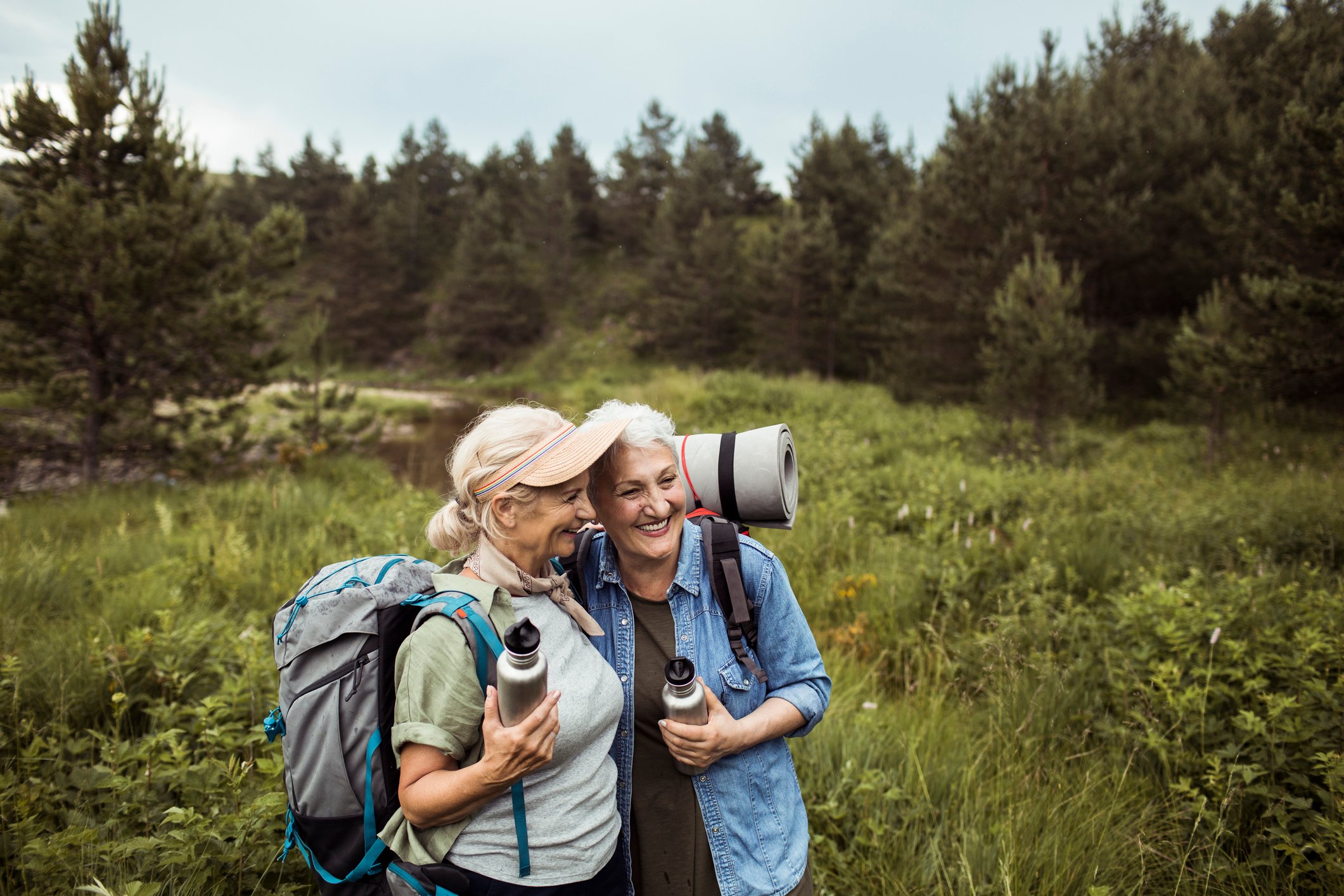 Two adults in field with backpacks and water bottles.