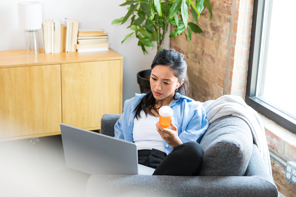Person on couch holding plastic container while utilizing personal computing device.