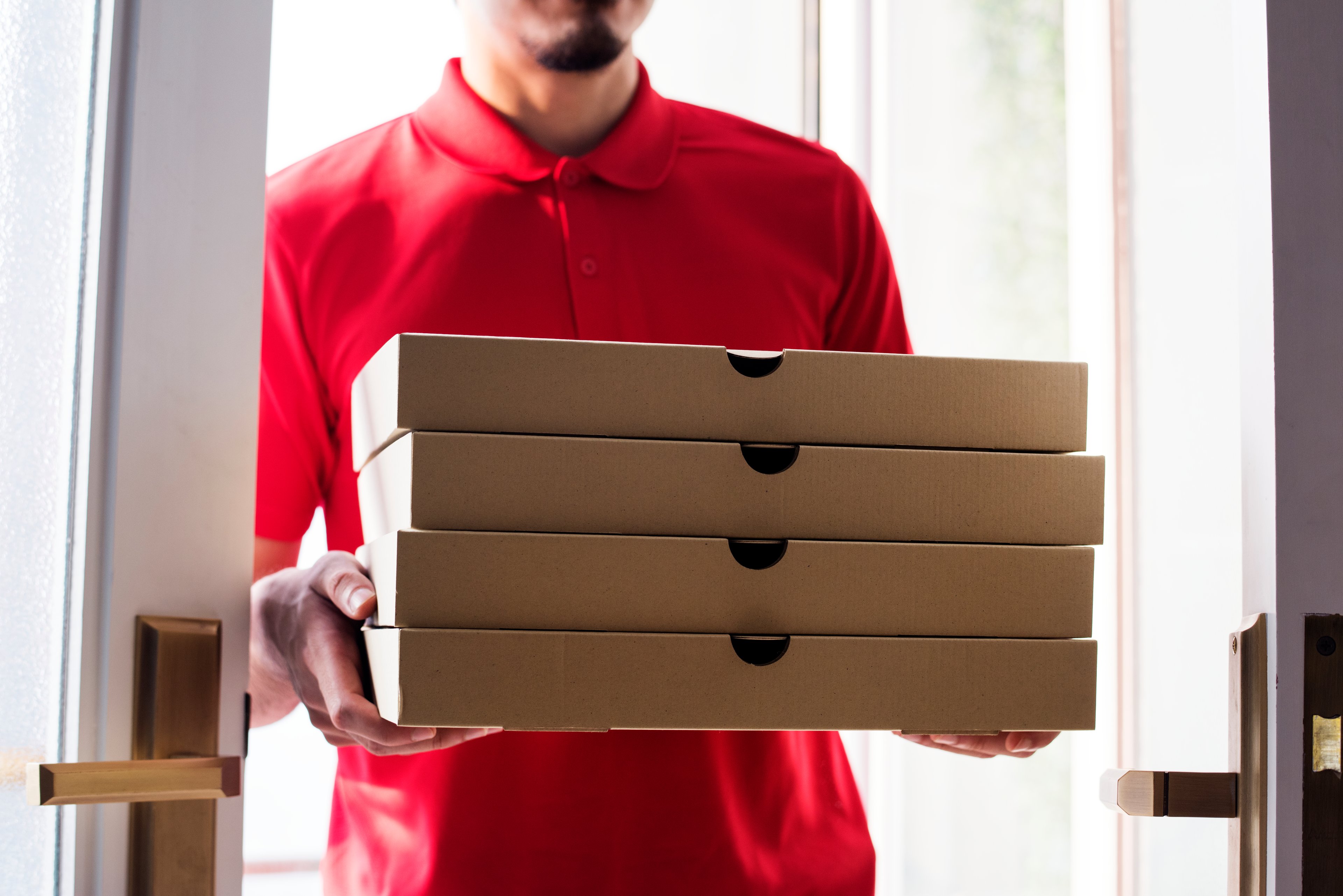 A delivery person drops off four boxes of pizza at a residence, with the picture showing them standing just inside the doorway.