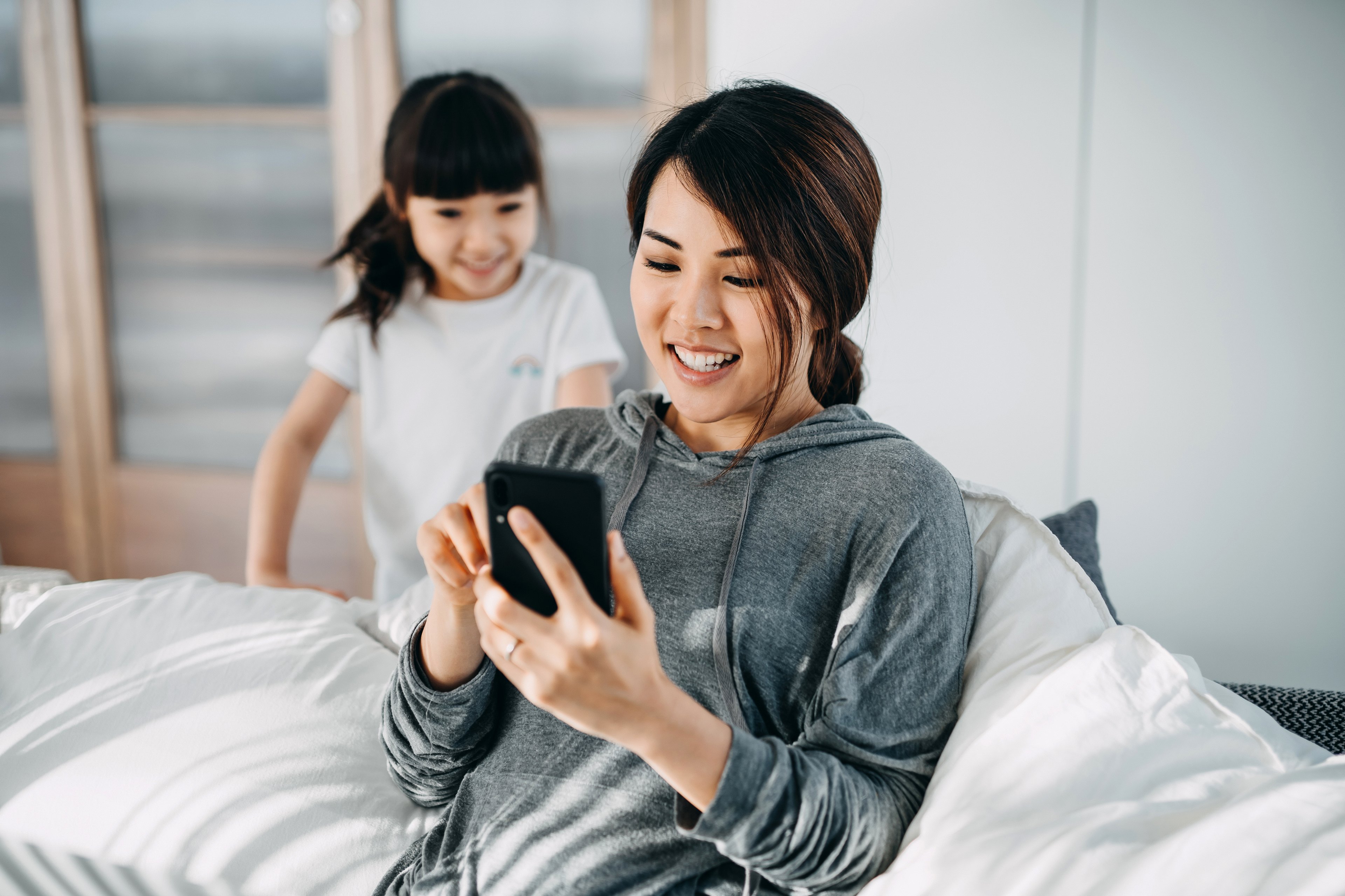 Young Chinese mother on smartphone with daughter. 