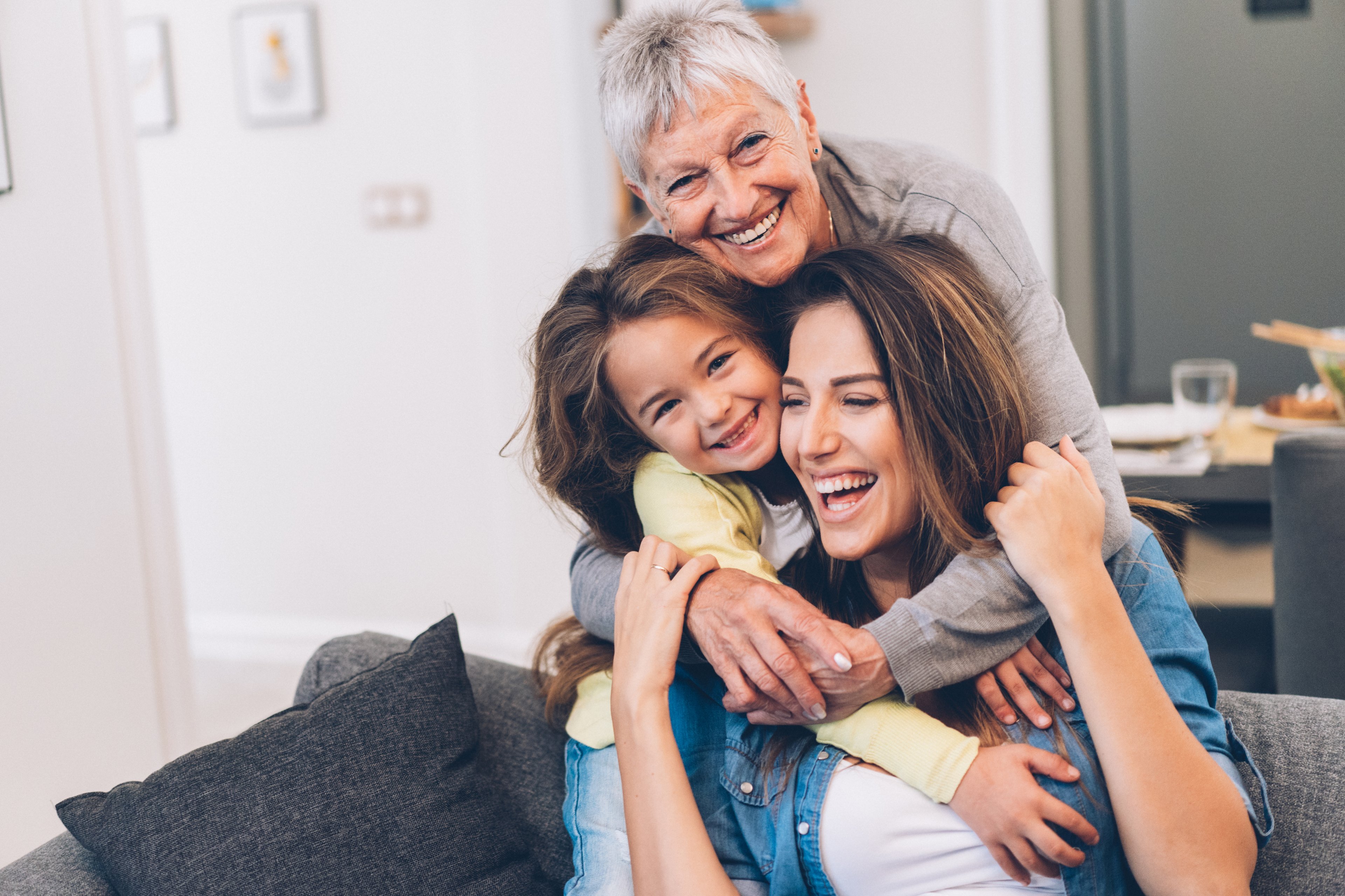 Three people hugging while on a couch.