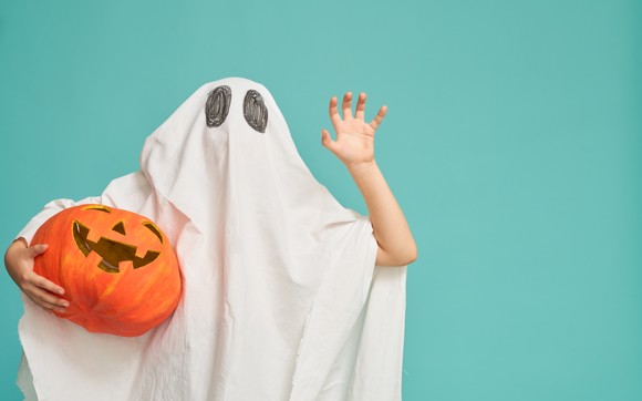 Someone in a ghost costume holding a jack-o-lantern.